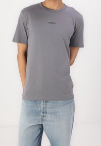 Grijze katoen t-shirt met een ronde halslijn en een klein zwart 'REPLAY' logo in het midden. Gecombineerd met lichtblauwe jeans.