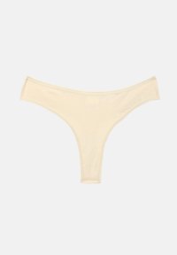 String en coton beige pour femme avec côtés étroits et ceinture taille basse sur fond blanc.