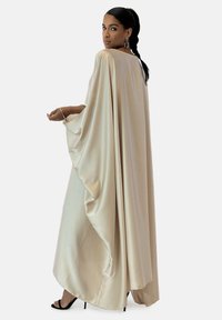 Beige satin klänning med en flödande silhuett, breda ärmar och en samlingsdetalj på baksidan. I kombination med svarta högklackade sandaler.