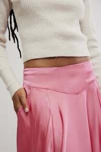 Falda de satén rosa con cinturilla ajustada, bolsillos laterales y forma fluida. La persona que la lleva viste un suéter de canalé color beige claro.