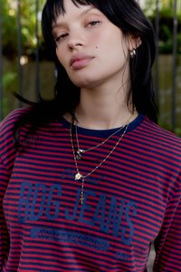 Cămașă cu dungi roșii și bleumarin, cu un imprimeu grafic. Sunt vizibile mai multe coliere aurii cu pandantive diverse și cercei.