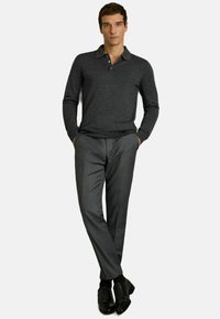 Cămașă polo gri închis cu guler și trei nasturi, asociată cu pantaloni gri eleganți și pantofi din piele negri, stând cu mâinile în buzunare.