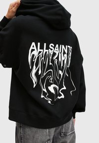 Černá mikina s kapucí s velkým bílým grafickým designem se textem "ALLSAINTS" a abstraktními tvary na zádech. Měkká textura látky.
