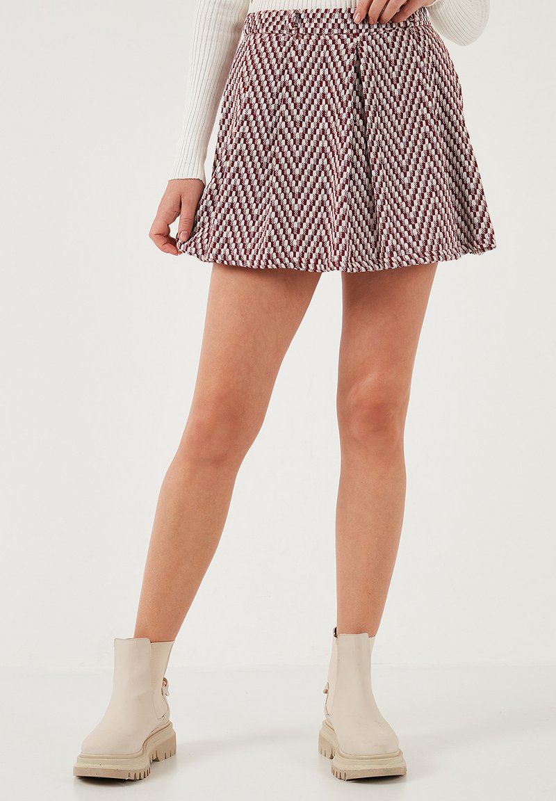 Una gonna skater a zigzag bordeaux e bianca con un cinturino arricciato, abbinata a stivaletti beige con suola spessa.