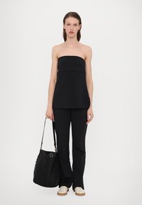 Svart stroppeløs topp med en sømløs design, kombinert med svarte skreddersydde bukser. En vevd svart bøtteveske og beige joggesko fullfører antrekket.