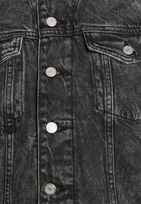 Svart denimjacka med silverfärgade tryckknappar, två bröstfickor och synliga söm detaljer. Tyget verkar något slitet.