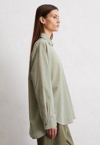Light green oversized shirt made of soft fabric, featuring a button-up front, pointed collar, and long sleeves with buttoned cuffs.