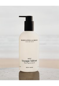 Bouteille en verre transparent avec un bouchon-pompe noir ; étiquetée "N°07 Voyage Vétiver" avec un texte simple sur une finition légèrement givrée.