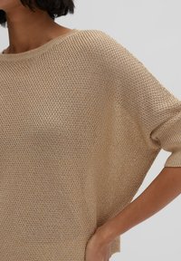 Beige gestrickter Pullover mit lockerer Passform, weitem Ausschnitt und kurzen Ärmeln. Texturiertes Gewebe mit offenem Webmuster.