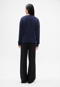 Granatowy sweter z okrągłym dekoltem i długimi rękawami, w połączeniu z czarnymi spodniami o szerokich nogawkach. Gładki materiał, luźny krój, minimalistyczny design.
