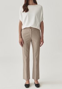 Top blanco y holgado con pantalones beige rayados de pierna recta. Los pantalones cuentan con un cierre frontal de botón y una textura sutil. Bailarinas negras.