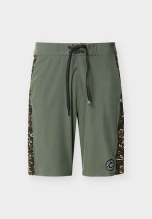 Olívazöld fürdőnadrág fekete húzózsinórral, terepmintás oldalpanelek, valamint kerek fekete-fehér logófolt a szegély közelében.