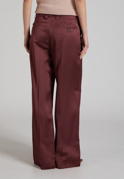 Vista trasera de una persona que lleva pantalones de satén de talle alto y pierna ancha en burdeos profundo con bolsillos traseros abotonados, combinados con una blusa beige texturizada.