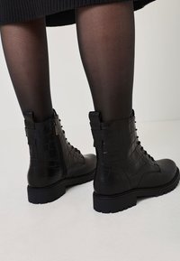 Schwarze Stiefel aus Kunstleder im Kampfstil mit strukturiertem Krokodil-Muster, Schnürung vorne und seitlichem Reißverschluss. Gummisohlen für zusätzlichen Halt und Langlebigkeit.