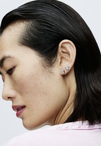 Strieborné náušnice so vzorovaním, ktoré majú dva odlišné dizajny na každom uchu. Hladký, lesklý povrch s reflexnými plochami.