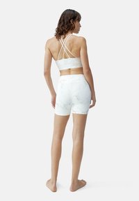 Top sportivo bianco con motivo in marmo, dotato di bretelle incrociate, abbinato a pantaloni corti a vita alta, entrambi realizzati in tessuto morbido ed elasticizzato.