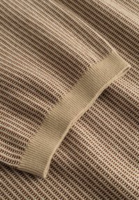 Beige ja pruuniga tekstureeritud kootud kangas lähedalt, kampsuni varruka soonikkoes manseti detailiga.