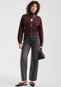 Maglione borgogna con zip e motivo a texture, abbinato a jeans scuri a vita alta. L'accessorio include una sciarpa nera e una borsa piccola.