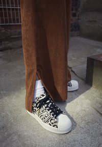 Czarno-białe trampki w geometryczne wzory z fakturowanym materiałem, białym gumowym noskiem i czarnymi sznurowadłami. Brązowe spodnie sztruksowe z bocznymi rozcięciami.