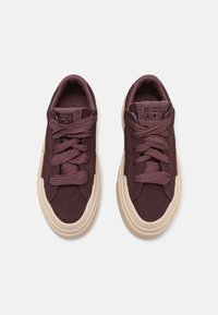 Nízké tenisky Converse All Star v tmavě fialovém semiši s tlustými béžovými gumovými podrážkami a ladícími fialovými tkaničkami, pohled zhora.