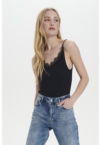 Must värviline soonikuga top, mille kaeluses on pitsäär, paari kõrge vöökoha siniste denim teksadega, mis omavad klassikalist viit tasku.