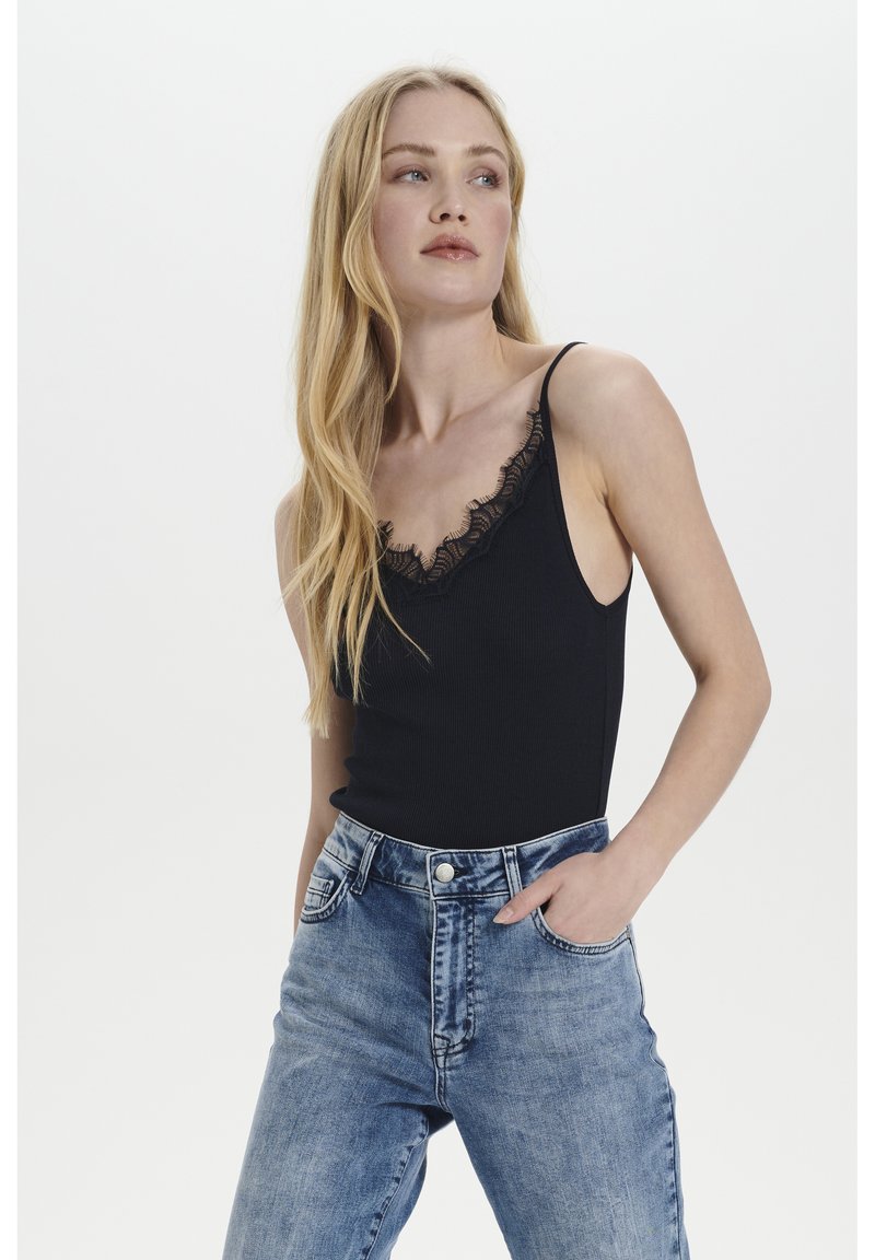 Must värviline soonikuga top, mille kaeluses on pitsäär, paari kõrge vöökoha siniste denim teksadega, mis omavad klassikalist viit tasku.