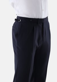 Marineblaue Hosen mit plissiertem Design, ausgestattet mit einer Knopfverschluss und verstellbaren Bundlaschen, gefertigt aus glattem Stoff.