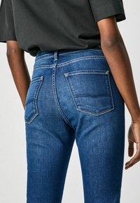 Blå denimjeans med en figursydd design, synliga bakfickor, kontrasterande sömmar och mjuk textur. Bärs med en lös svart topp.