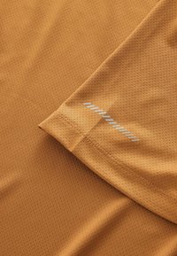 Pomarańczowa sportowa koszulka z teksturowaną siateczkową tkaniną. Posiada kontrastujący srebrny akcent na ramieniu dla dodatkowego efektu.