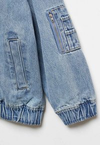 Denim jakna u svijetloplavoj boji s džepom na patentni zatvarač i bočnim flap džepovima. Ima elastične manžete i opuštenu siluetu. Mekani tekstur.
