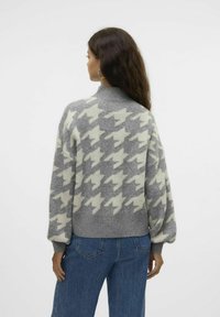 Šviesiai pilka vilnos megzta palaidinė su houndstooth raštu. Dėl aukštos apykaklės ir plačių, pūslinių rankovių atrodo stilingai. Dėvima su mėlynomis džinsinėmis kelnėmis.
