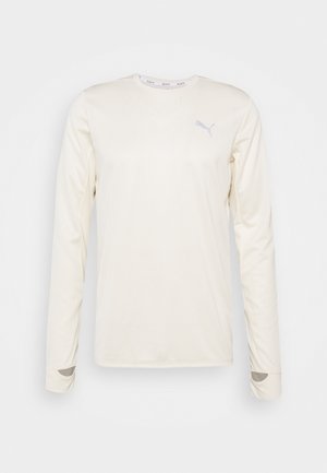 T-shirt de sport à manches longues de couleur crème avec un col rond, une texture côtelée et un petit logo réfléchissant sur la poitrine.