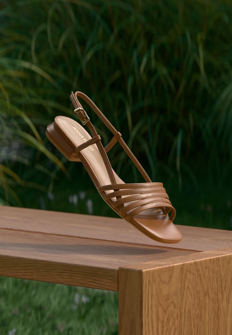 Sandale pour femme en cuir marron à bout ouvert avec fines lanières et boucle à la cheville, reposant sur le bord d'un banc en bois en plein air.