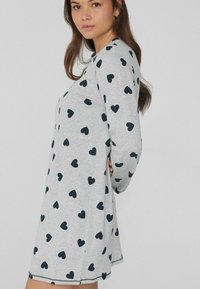 Abito grigio a maniche lunghe con motivi a cuore blu navy, materiale morbido, scollo rotondo e spacchi laterali all'orlo per facilitare i movimenti.