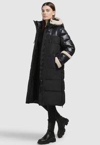 Schwarze Daunenjacke mit Kapuze, ausgestattet mit einem weichen beigen Innenfutter am Kragen und an den Bündchen, Reißverschluss und Seitentaschen. Stilvolles knielanges Design.