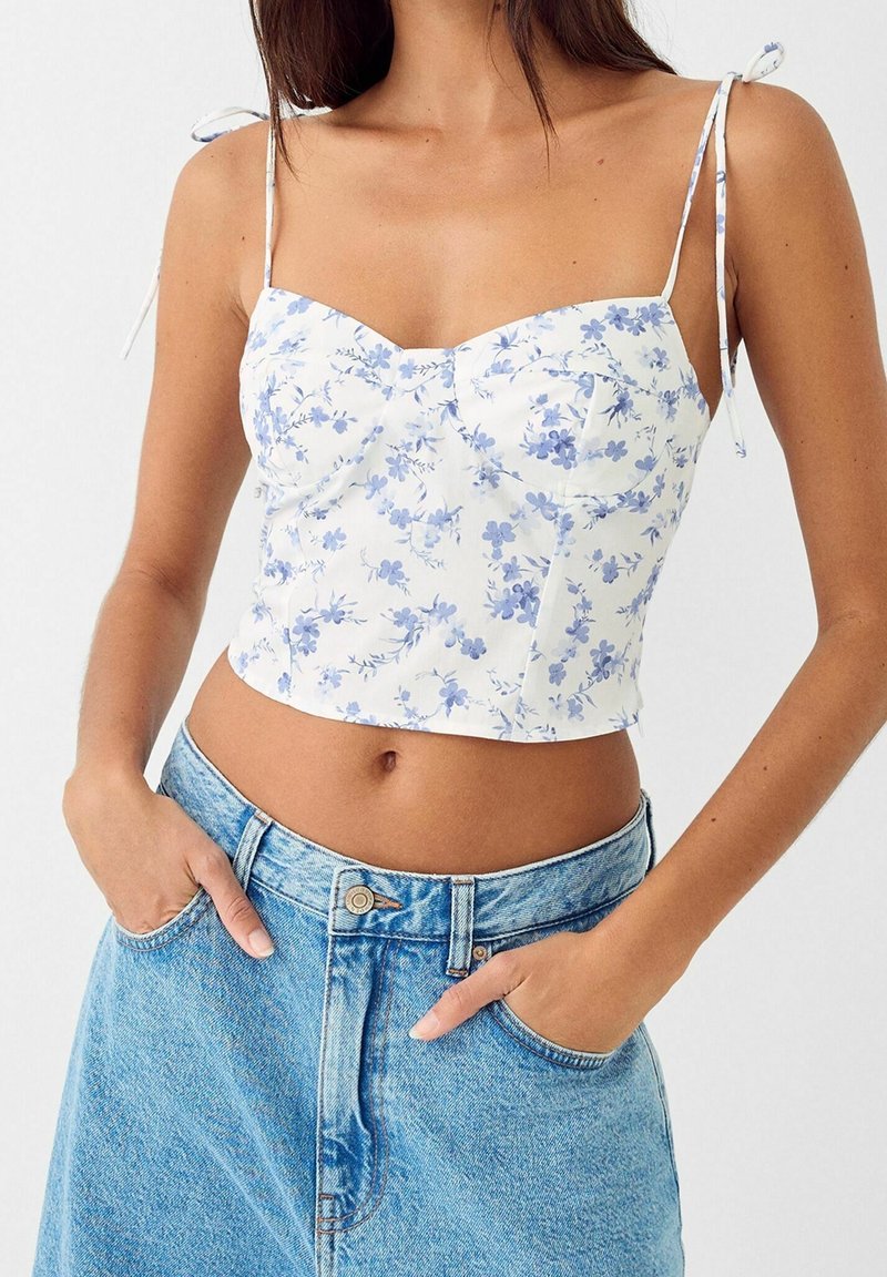 White cropped top with blue floral print, featuring a sweetheart neckline, adjustable spaghetti straps, and a fitted silhouette.