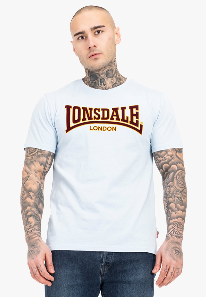 Šviesiai mėlynas medvilninis marškinėlis su dideliu tamsiai raudonu "Lonsdale London" logotipu. Trumpomis rankovėmis ir apvaliu kaklu. Minimalistinis dizainas.