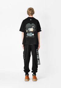 Camiseta negra de gran tamaño con estampado gráfico en la parte posterior; combinada con pantalones cargo negros con bolsillos laterales y botas de tobillo naranjas.