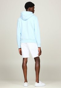 Sudadera con capucha de color azul claro con puños y dobladillo acanalados, combinada con pantalones cortos blancos y zapatillas blancas. Textura suave, corte relajado.