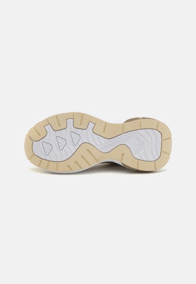 Sneaker-sula med en vit bas, en texturerad, beige mellansula och ett mönstrat slitban för grepp. Märkbara logotyper präglade.