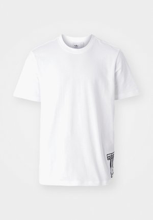 Bela bombažna majica s kratkimi rokavi, okroglim izrezom in črno oznako Adidas na spodnji levi strani. Gladka tekstura.