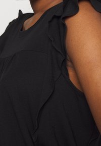 Czarna bluzka z falbaniastymi detalami na ramionach, miękkiego materiału, z okrągłym dekoltem i rozkloszowanym dołem, idealna na co dzień.