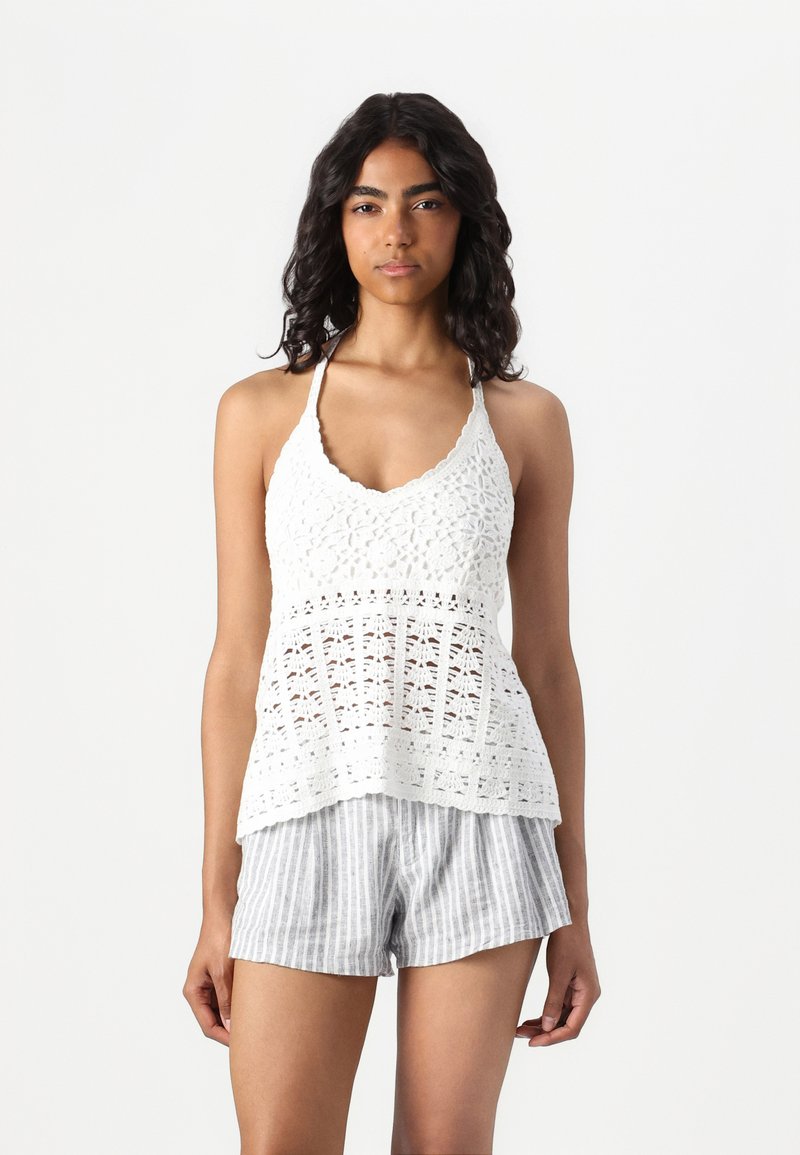 Hvitt heklet tanktop med scalloped hals og åpen blondedesign, sammen med gråstripete shorts.