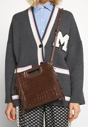 Sac en cuir de crocodile marron estampé avec des accents de frange, surface texturée, anse supérieure et bandoulière amovible, porté à côté d'un cardigan gris.