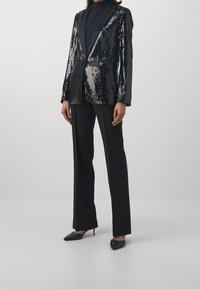 Blazer negro con lentejuelas y solapa de satén, de un solo botón y dos bolsillos frontales, combinado con pantalones negros a medida y tacones negros de punta.