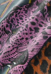 Gewebe mit lila Leopardenmuster und schwarzen Flecken auf einem strukturierten Hintergrund, kombiniert mit einem Detail aus orangefarbenem und braunem Tiermuster.