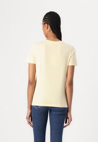 Lys gul kortermet t-skjorte med rund hals, myk tekstur og tettsittende form, kombinert med mørkeblå jeans.
