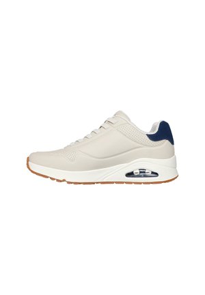 Beige Sneaker mit einem glatten synthetischen Obermaterial, navy Akzenten, perforierten Details, weißer Zwischensohle und sichtbarer Air-Dämpfung in der Ferse.