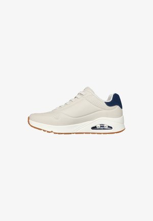 Beige Sneaker mit einem glatten synthetischen Obermaterial, navy Akzenten, perforierten Details, weißer Zwischensohle und sichtbarer Air-Dämpfung in der Ferse.