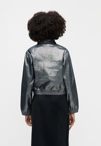 Metalikno siva kratka jakna s elastičnim pojasom i manžetama, s glatkom teksturom i klasičnim ovratnikom.